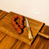 Tabla de madera con cuchillo que recuerdan a pueblo junto a Chorizos caseros de pincho picantes Arrrea.