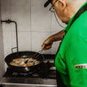 Hombre friendo lomo en sartén en una cocina de pueblo de manera artesanal.